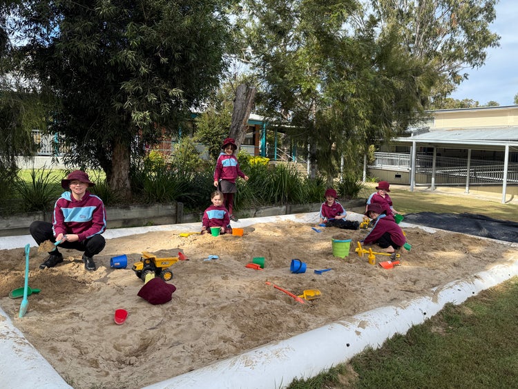 A photo of six student playing in a large sandpit in school grounds